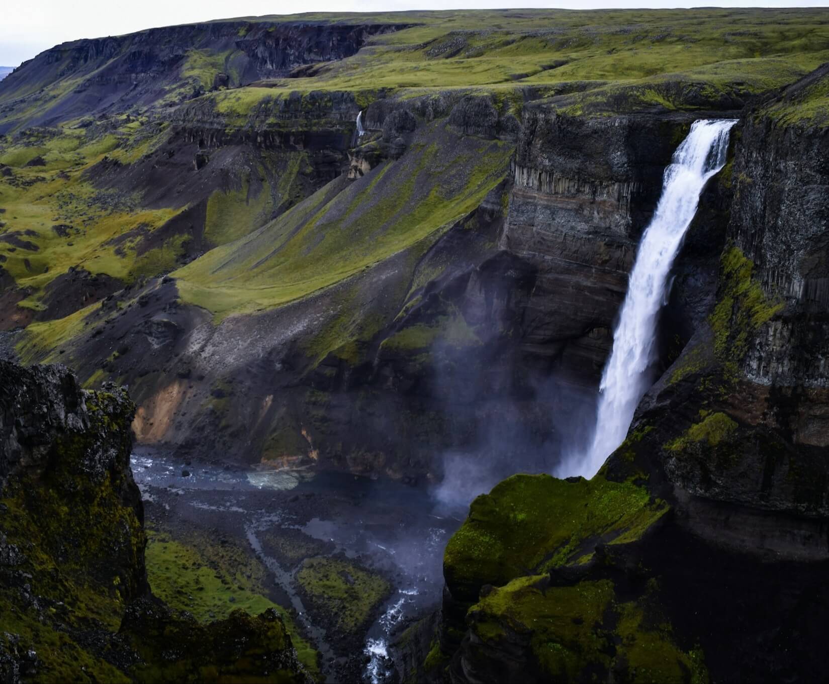 Waterfall over green cliffs into a river