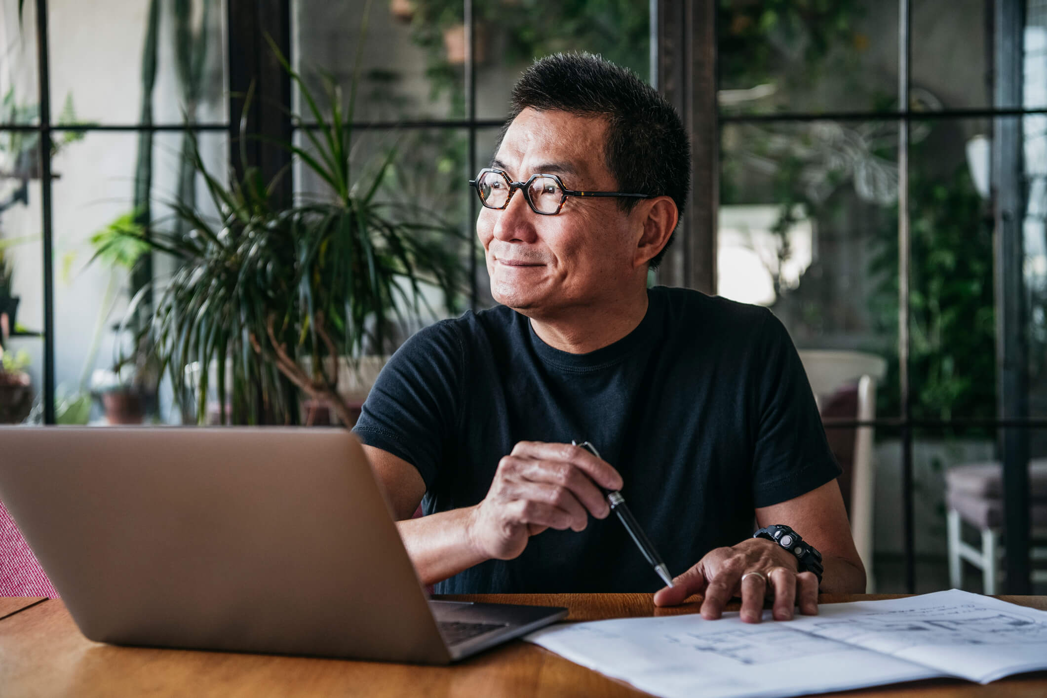 A mature man looks over paper and computers at his table.